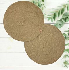 two round placemats sitting on top of a white wooden floor next to green leaves