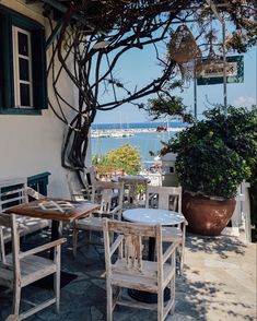 an outdoor table and chairs on a patio next to a tree with boats in the background