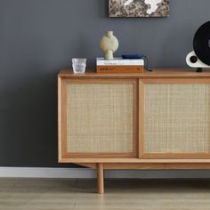 a wooden sideboard with speakers on top of it next to a painting and vase