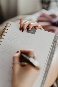 a woman's hands holding a calendar and pen on top of a book that is open