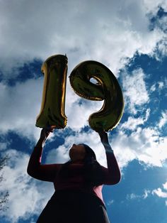 a woman holding up two large balloons in the shape of the number nine on her head