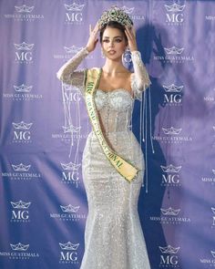 a beautiful woman in a white dress posing for the camera with a crown on her head