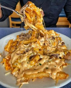 a person eating french fries covered in gravy on a plate with a fork