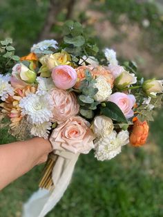 a bridal bouquet being held by someone's hand on the grass in front of them