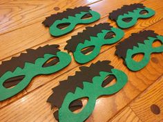 some green and black masks on a wooden floor with holes in the middle to cut them out