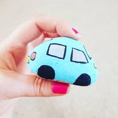 a hand holding a rock with a small car painted on it's side and pink nail polish