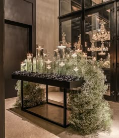 a table with candles and plants in front of a glass case filled with wine glasses