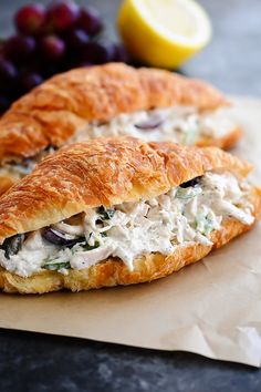 two croissants filled with chicken salad on top of wax paper next to grapes