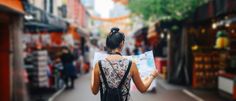 a woman is walking down the street with a map in her hand and looking at shops