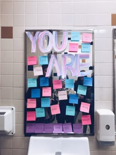 a mirror with post it notes attached to the side of it in front of a urinal