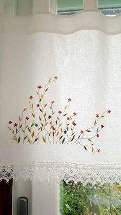 a white curtain with red and blue flowers on it next to a window sill