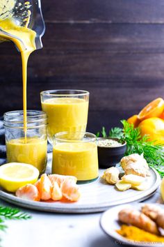 orange juice being poured into small glasses on a plate with lemons and other fruits