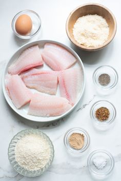 fish fillets and ingredients laid out on a white countertop with bowls, eggs, flour, and measuring spoons