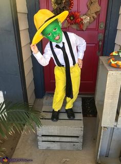 a person in a green mask and yellow pants standing on steps with a red door