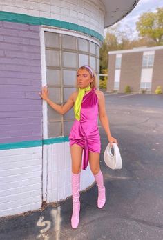 a woman in pink and yellow is leaning against a building with her hand on the door