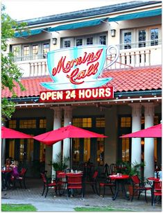 an outdoor restaurant with red umbrellas and tables in front of the building that says morning cafe open 24 hours