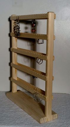 a wooden rack with rings and bracelets hanging from it's sides on a white surface