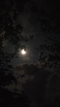 the moon shines brightly through the clouds in the night sky above trees on a cloudy day