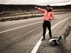 a man standing on the side of a road pointing at something in the air with his arms outstretched