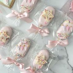 pink decorated cookies in plastic wrappers on a marble counter top with bows and sprinkles