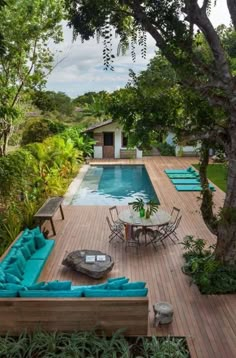 an outdoor deck with couches and tables next to a swimming pool in the woods