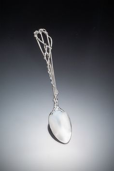 a silver spoon with a chain hanging from it's side on a gray background