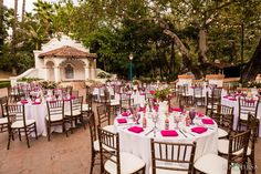 tables and chairs are set up for an outdoor wedding reception with pink linens on them