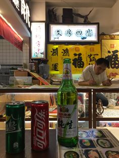 a man sitting at a table in front of a bottle of beer and two cans of soda