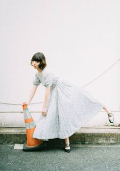 a woman in a white dress leaning on an orange cone