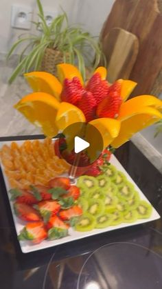 a plate with strawberries, oranges and other fruits on it next to a vase filled with flowers