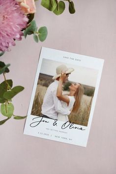 a wedding save the date card with pink flowers and greenery in front of it