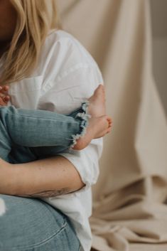 a woman holding a baby in her arms while sitting on a couch with a white sheet behind her