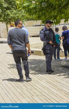 two police officers talking to each other in front of some people on the sidewalk with trees