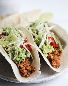 three tacos on a plate with shredded lettuce and tomato sauce in the middle