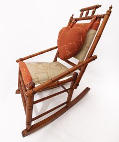 a wooden rocking chair with an orange pillow on it's back and seat cushion