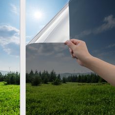 a person holding up a piece of paper in front of a field with trees and blue sky