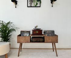 an old record player sits on a wooden table in front of a white wall with plants