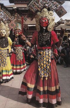 some people are dressed up and dancing in costumes with masks on their faces, while others look on