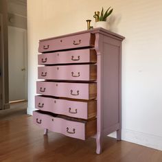 a pink dresser sitting on top of a hard wood floor next to a white wall