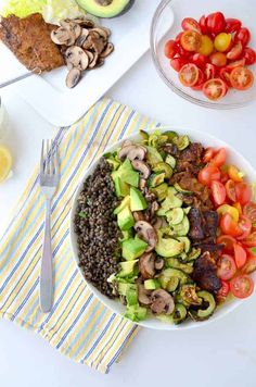 a white plate topped with vegetables and meat next to a bowl of salad on a table