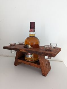 a bottle of whiskey sitting on top of a wooden stand with shot glasses next to it