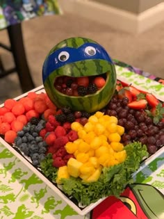 a watermelon shaped like a turtle sitting on top of a table filled with fruits and vegetables