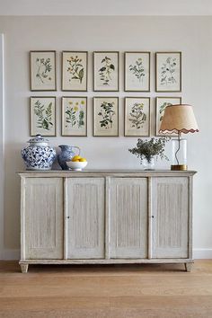 a white cabinet with pictures on the wall above it and a lamp next to it