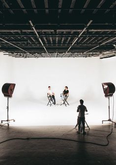 three people sitting on chairs in front of a white backdrop with lights and lighting equipment