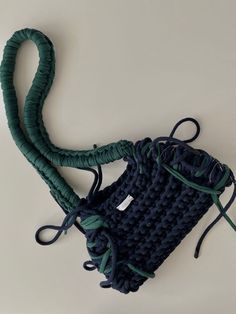 a crocheted bag with a cord attached to the front and side, sitting on a white surface