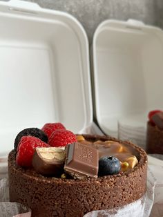 a chocolate cake with berries, raspberries and other toppings in a plastic container