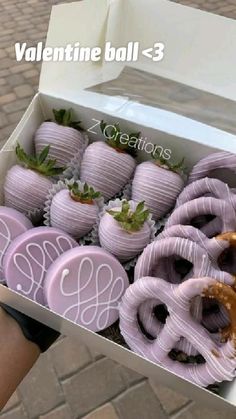 a person holding a box full of purple chocolate covered strawberries and pretzels