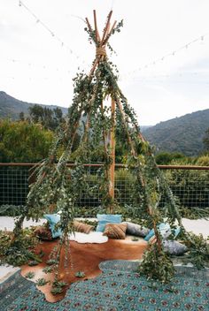 an outdoor seating area is decorated with greenery and pillows on the floor, along with string lights