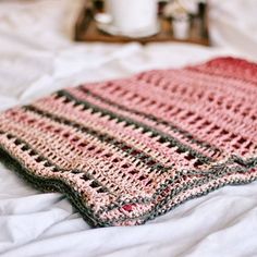 a crocheted blanket laying on top of a bed next to a cup of coffee