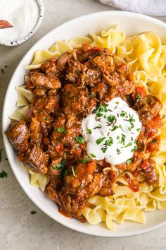 a white bowl filled with pasta and meat covered in sauce, topped with sour cream